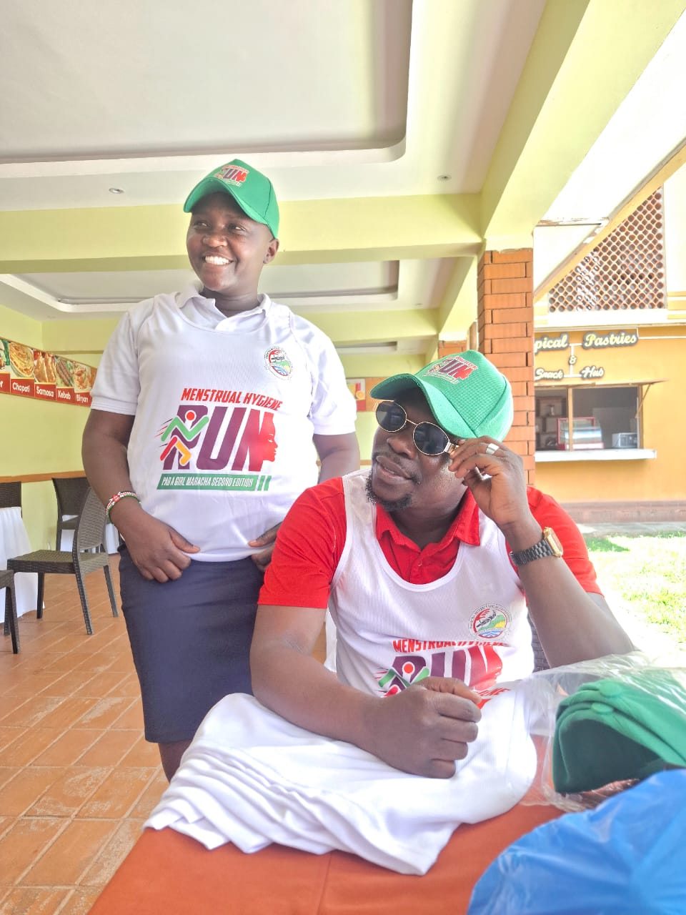 Two people wearing menstrual hygiene run shirts and caps