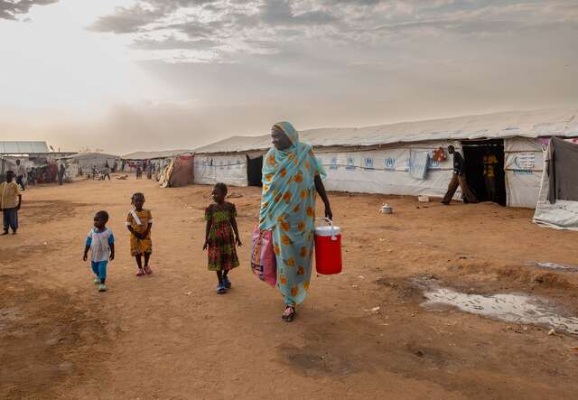 A Sudanese mother walking with children through a displacement camp